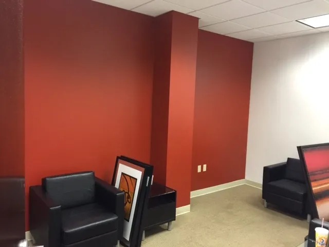 A red-walled office corner with black chairs and framed pictures.