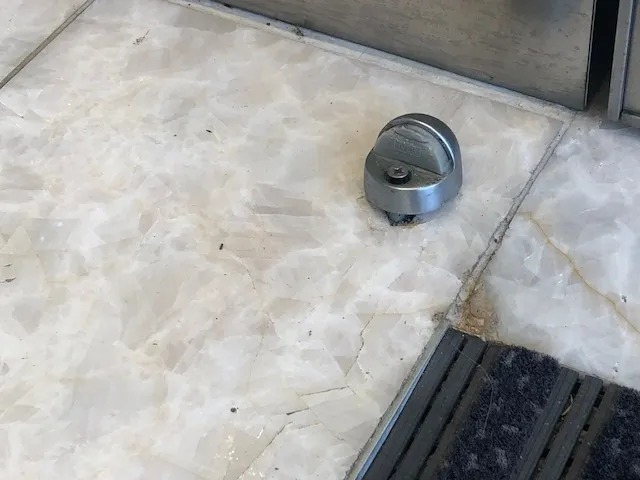 Ceiling-mounted surveillance camera on a concrete surface near a door mat.