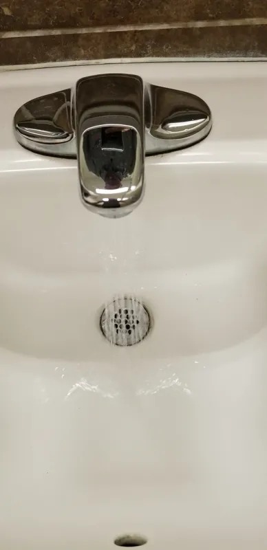 Water flowing from a faucet into a white sink.