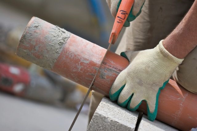 A worker cutting a rusty pipe with a handheld saw.