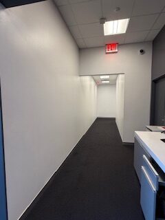 A narrow office hallway with white walls and dark flooring.