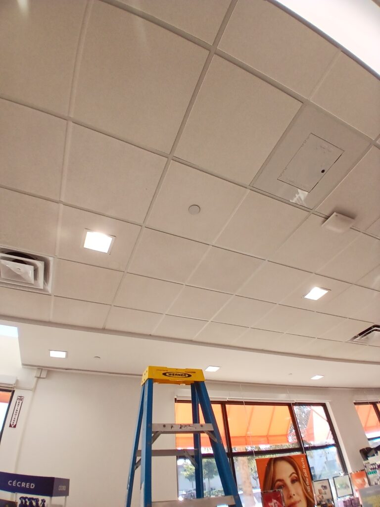 A ladder set up in a white ceiling room with recessed lighting and ceiling vents.