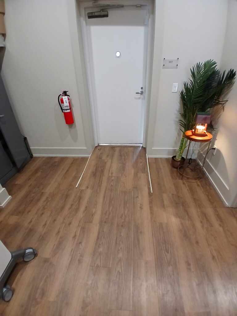 A clean room corner with wooden floor, white walls, and a small plant on a round wooden table.