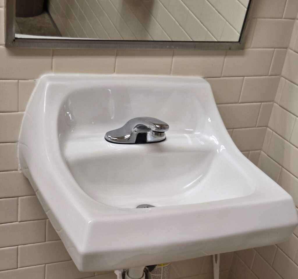 White ceramic bathroom sink with a single faucet and tiled wall.