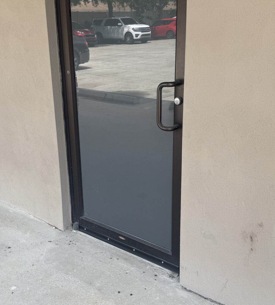 Black metal door with glass panel in a concrete wall.