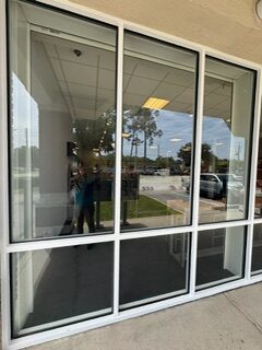 Reflection of a person taking a photo in a glass door with outdoor scenery.