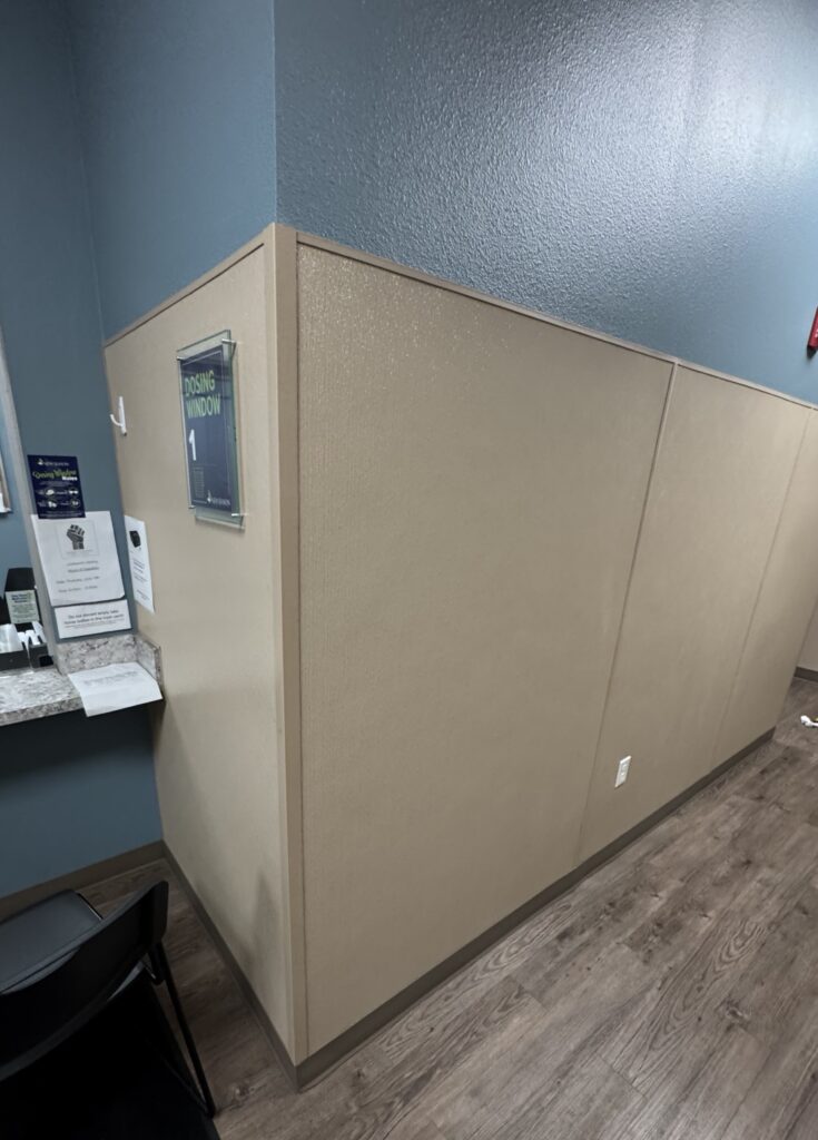 A beige office cubicle with a small window and nearby workspace.